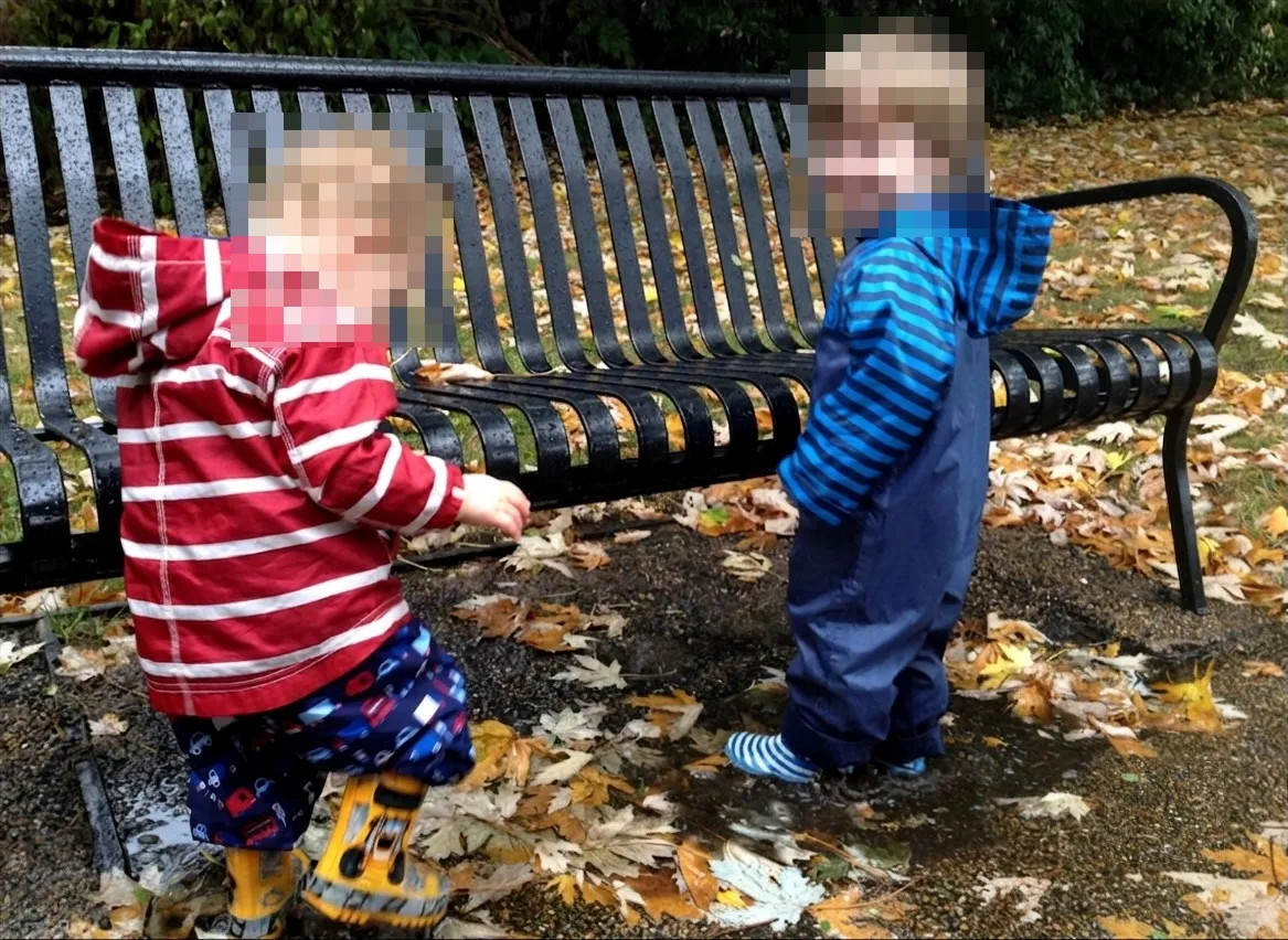 Two children wearing puddle suits and splashing in a puddle.