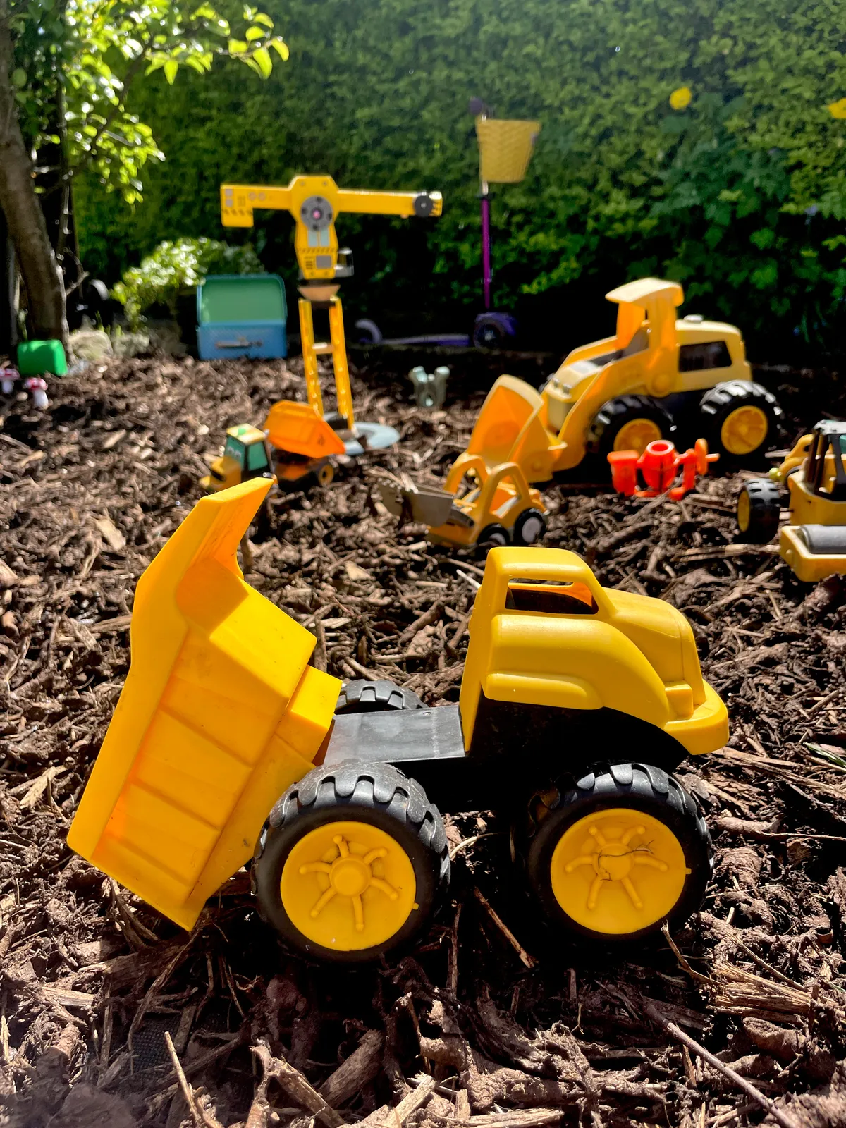 Digger toys and a wooden crane outside in bark